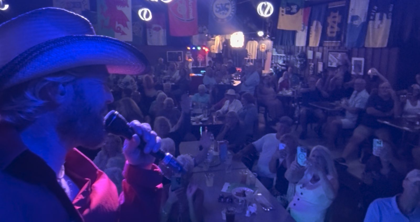 View from the stage: Joshua Alan singing to a packed room, people singing along and filming on their phones