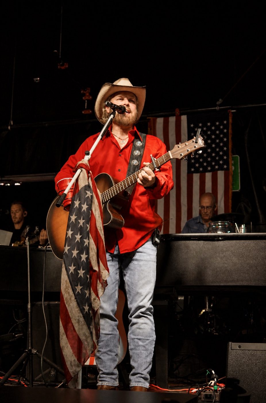 Joshua Rupp in a red shirt performing with an American flag on the mic stand